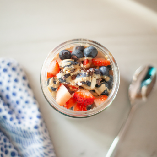 Macro-friendly, filling cauliflower oats with toppings in a jar and a spoon to the side.