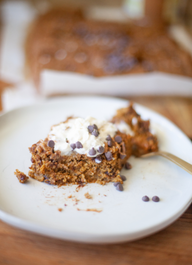 Protein pumpkin dessert on a white plate topped with cream cheese frosting and chocolate chips.