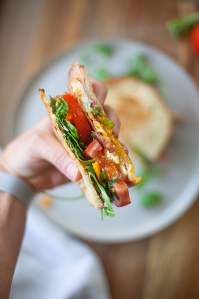 Hand holding half of a fried egg BLT