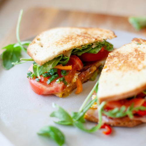 Fried egg blt sandwich cut in half on a white plate.