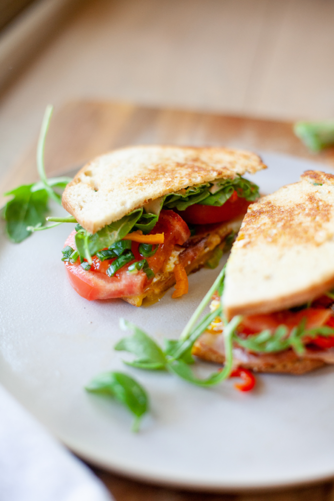 Fried egg blt sandwich cut in half on a white plate.