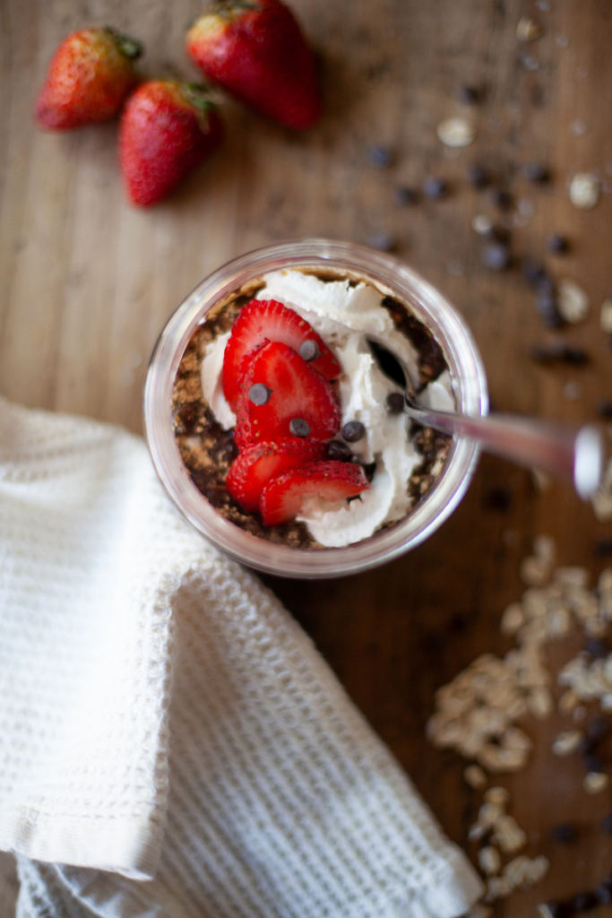 Chocolate protein overnight oats with whipped cream and strawberries on top.