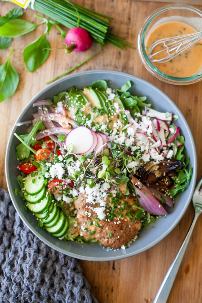 Large bowl of salad next to a small glass container of chipotle vinaigrette.
