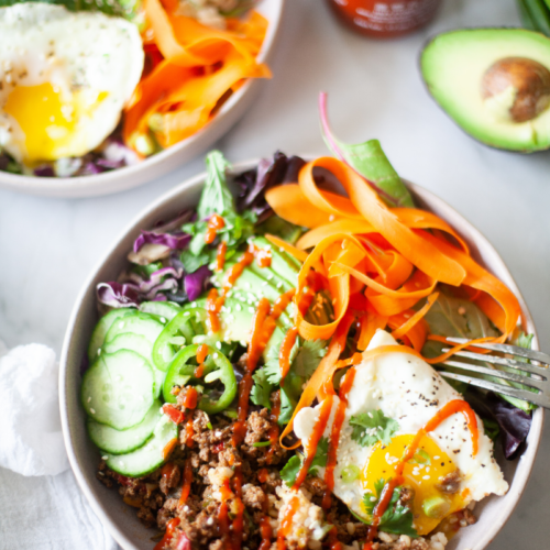 Assembled korean beef bowl in large white bowl drizzled with sriracha and fork on the side.