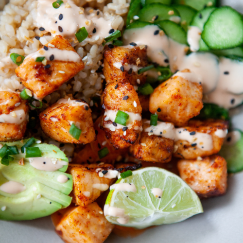 Air fryer salmon bites on top of rice and sliced cucumber.