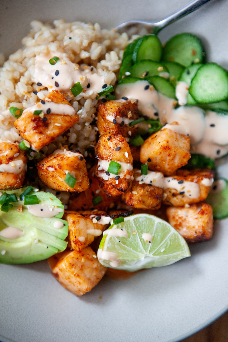 Air fryer salmon bites on top of brown rice with cucumbers, chives, avocado, and lime.