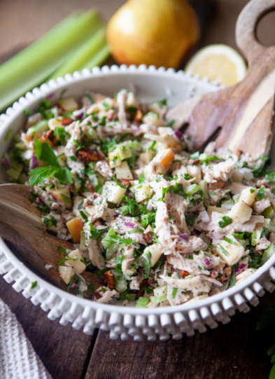 Waldorf chicken salad in large mixing bowl with wooden mixing spoon.