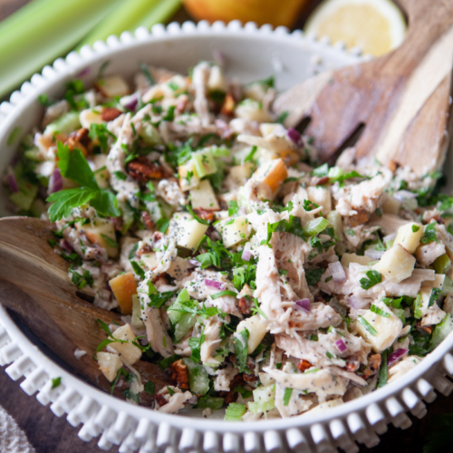 Waldorf chicken salad in large mixing bowl with wooden mixing spoon.