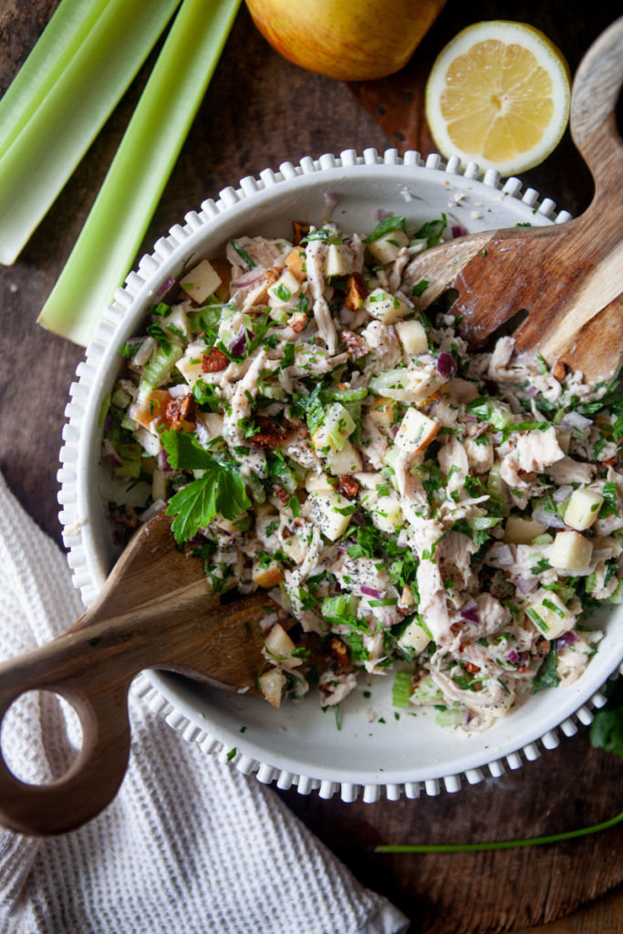 Macro-friendly waldorf chicken salad in white mixing bowl with two wooden spoons.