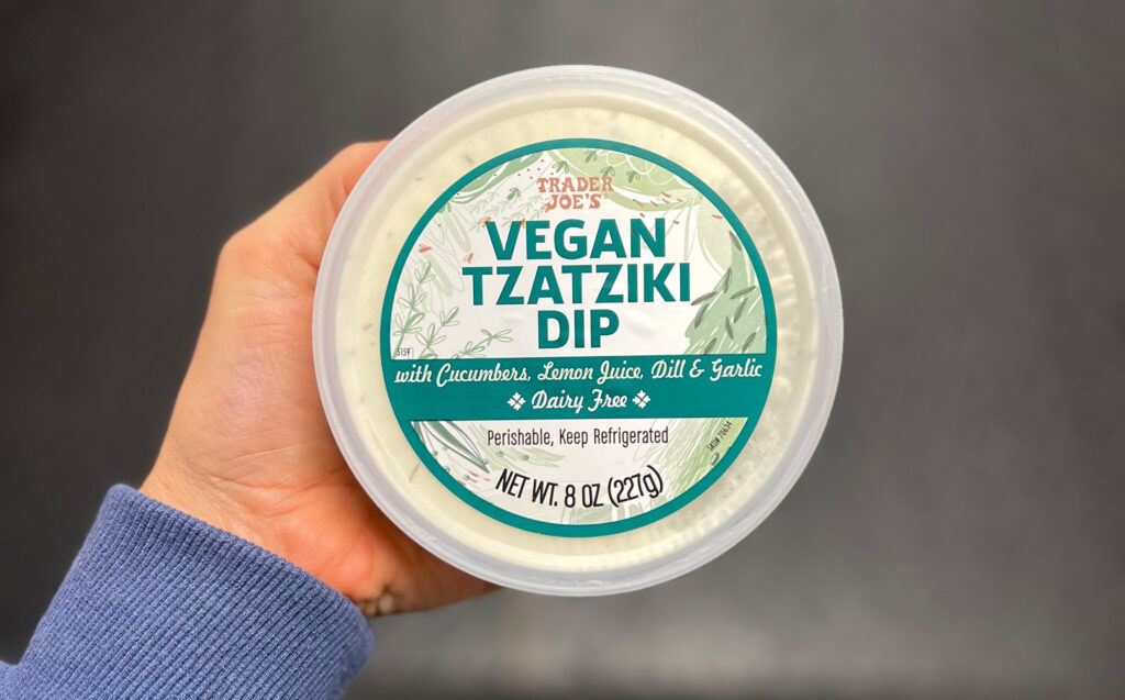 A hand holds a container of Trader Joe’s Vegan Tzatziki Dip with cucumbers, lemon juice, dill, and garlic—one of My Favorite Trader Joe’s Products. The label notes it is dairy-free, 8 oz (227g), and should be kept refrigerated.