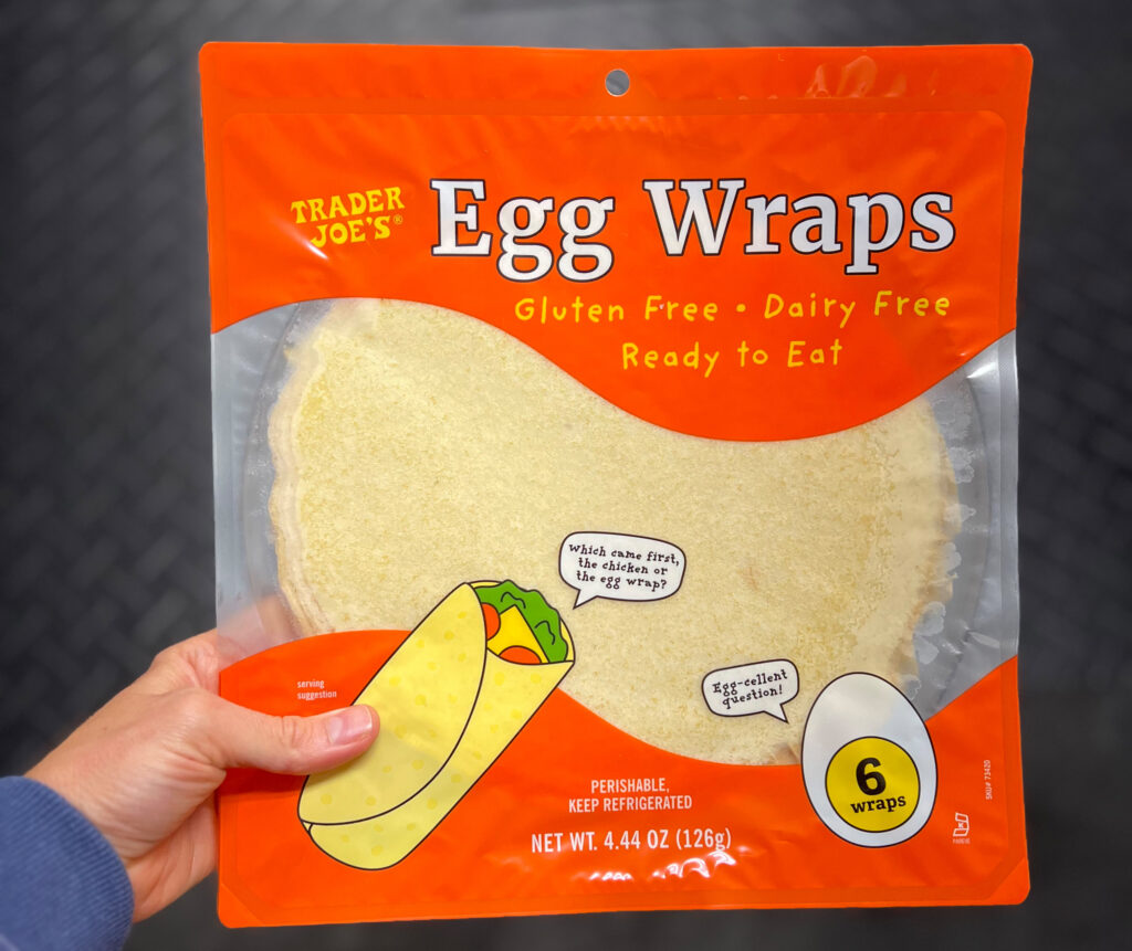 A hand holds a package of Trader Joe’s Egg Wraps, one of My Favorite Trader Joe’s Products. The orange package says Gluten Free • Dairy Free • Ready to Eat and contains six wraps. There’s an illustration of a taco and an egg on the front.