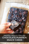 A hand holds a delicious chocolate pumpkin snack cake square above a tray filled with more chocolate pumpkin snack cakes. Text reads: Healthy, Macro-friendly Chocolate Pumpkin Snack Cakes.