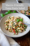 A bowl of vibrant tuna pasta salad with vegetables and herbs is served on a table with a fork. Text overlay reads Macro-Friendly Tuna Pasta Salad. Website lillieeatsandtells.com is displayed at the bottom.
