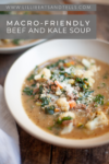 A bowl of Macro-Friendly Beef and Kale Soup with visible vegetables and ground beef, topped with grated cheese. The bowl sits on a wooden table with the text Macro-Friendly Beef and Kale Soup above.