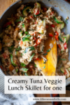 A skillet filled with a creamy tuna and veggie mixture, including red peppers and zucchini, with a wooden spatula resting inside. Text reads: Creamy Tuna Veggie Lunch Skillet for One—a perfect single-serving meal packed with flavor and wholesome ingredients.