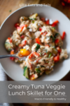 A close-up of a bowl filled with a rich Creamy Tuna Veggie Lunch Skillet for One, featuring tender tuna and colorful mixed veggies like red and yellow peppers, with a forkful lifted. Text reads Creamy Tuna Veggie Lunch Skillet for One.