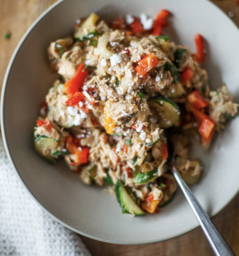 A bowl of shredded chicken mixed with zucchini, red bell peppers, and crumbled cheese, reminiscent of a Creamy Tuna Veggie Lunch Skillet for One, served with a fork on the side.