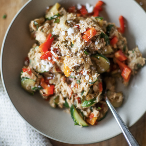 A bowl of shredded chicken mixed with zucchini, red bell peppers, and crumbled cheese, reminiscent of a Creamy Tuna Veggie Lunch Skillet for One, served with a fork on the side.