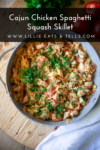 A skillet filled with Cajun Chicken Spaghetti Squash Skillet, topped with chopped parsley, sits on a wooden surface with fresh tomatoes nearby. Text overlay reads Cajun Chicken Spaghetti Squash Skillet.
