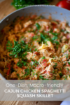 A skillet filled with creamy Cajun Chicken Spaghetti Squash Skillet, topped with chopped parsley, sits on a countertop. Text overlay reads: One-dish, macro-friendly Cajun Chicken Spaghetti Squash Skillet.