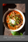 A bowl of Italian Pasta Soup topped with herbs and a dollop of cream, with a spoon in the bowl, sits on a table in sunlight. Text reads: One Dish Dinner Idea: Healthy Italian Pasta Soup.