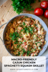 A skillet filled with Cajun Chicken Spaghetti Squash Skillet, featuring tender chicken, vibrant vegetables, and spaghetti squash, all topped with chopped parsley. Fresh tomatoes and herbs are arranged on the wooden surface beside the skillet. Text reads: Macro-Friendly Cajun Chicken Spaghetti Squash Skillet.