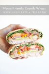 A hand holds two halves of a Macro-friendly Crunch Wrap filled with turkey, leafy greens, tomato, yellow bell pepper, and cheese. The wrap is sliced to show the colorful layers inside.