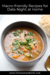 A bowl of hearty soup garnished with chopped herbs sits on a white surface next to a biscuit, with text above reading Date Night at Home Recipes: Macro-friendly dishes perfect for cozy evenings together.