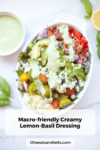 A white dish holds a colorful salad with cherry tomatoes, avocado, onions, feta, and a creamy Lemon-Basil Dressing, garnished with basil and lemon slices. Text: Macro-friendly Creamy Lemon-Basil Dressing.