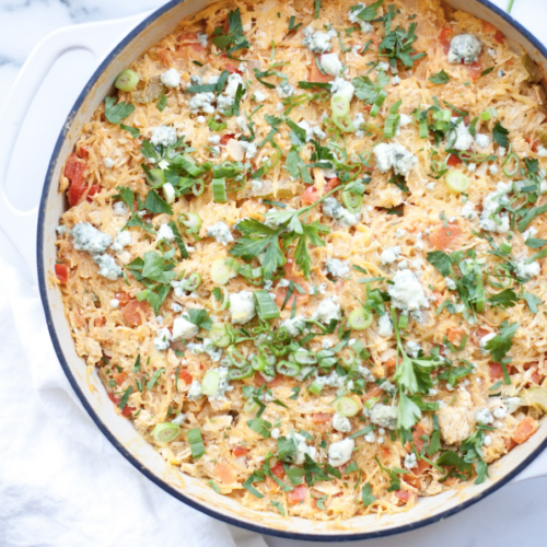 A large white pan filled with Buffalo Chicken Spaghetti Squash Casserole is topped with chopped green onions, parsley, and crumbled blue cheese, with visible bits of chicken and vegetables mixed in. A white napkin sits next to the pan.