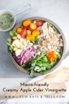A wooden bowl with quinoa, grilled chicken, cherry tomatoes, apple slices, red onion, greens, almonds, cheese, and an edible flower. A small bowl of creamy apple cider vinaigrette sits nearby for drizzling. Text: Macro-friendly Creamy Apple Cider Vinaigrette.