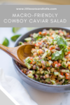A bowl of colorful Macro-friendly Cowboy Caviar Salad with diced vegetables and beans, garnished with cilantro, and a wooden spoon resting inside. The salad is labeled as macro-friendly.