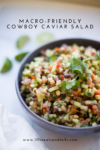 A bowl of colorful Macro-friendly Cowboy Caviar Salad with chopped vegetables and cilantro, set on a white surface with lime wedges in the background. Text overlay reads, Macro-Friendly Cowboy Caviar Salad.