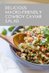 A bowl of colorful macro-friendly Cowboy Caviar Salad with beans, corn, and vegetables, garnished with cilantro, and a wooden spoon resting inside. Text on image reads, Delicious Macro-Friendly Cowboy Caviar Salad.