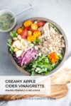 A bowl of salad with quinoa, apple slices, cherry tomatoes, red onion, chicken, arugula, and an edible flower is served alongside a cup of creamy Apple Cider Vinaigrette. Text reads: Creamy Apple Cider Vinaigrette.