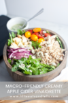 A wooden bowl filled with arugula, quinoa, red onions, cherry tomatoes, apples, nuts, blue cheese, and a side of creamy apple cider vinaigrette. Text overlay reads MACRO-FRIENDLY CREAMY APPLE CIDER VINAIGRETTE.