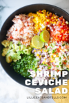 A bowl filled with chopped shrimp, avocado, onion, tomatoes, peppers, cilantro, and lime slices comes together to create a vibrant Shrimp Ceviche Salad. Text reads Shrimp Ceviche Salad and lillieeatsandtells.com.