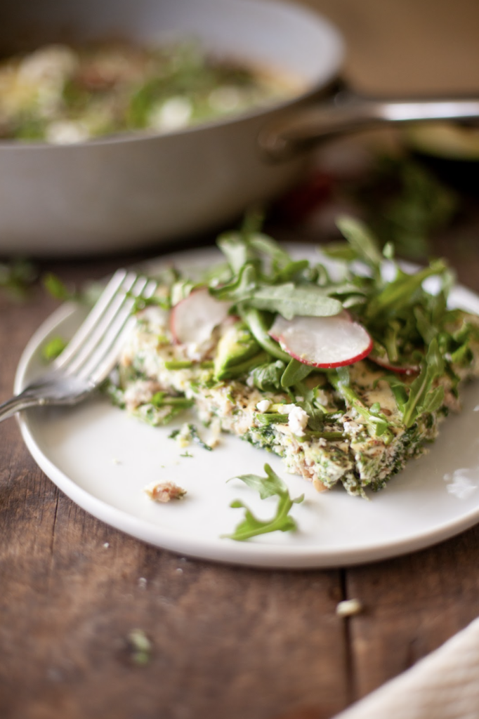 Slice of spring frittata on plate with fork and toppings.