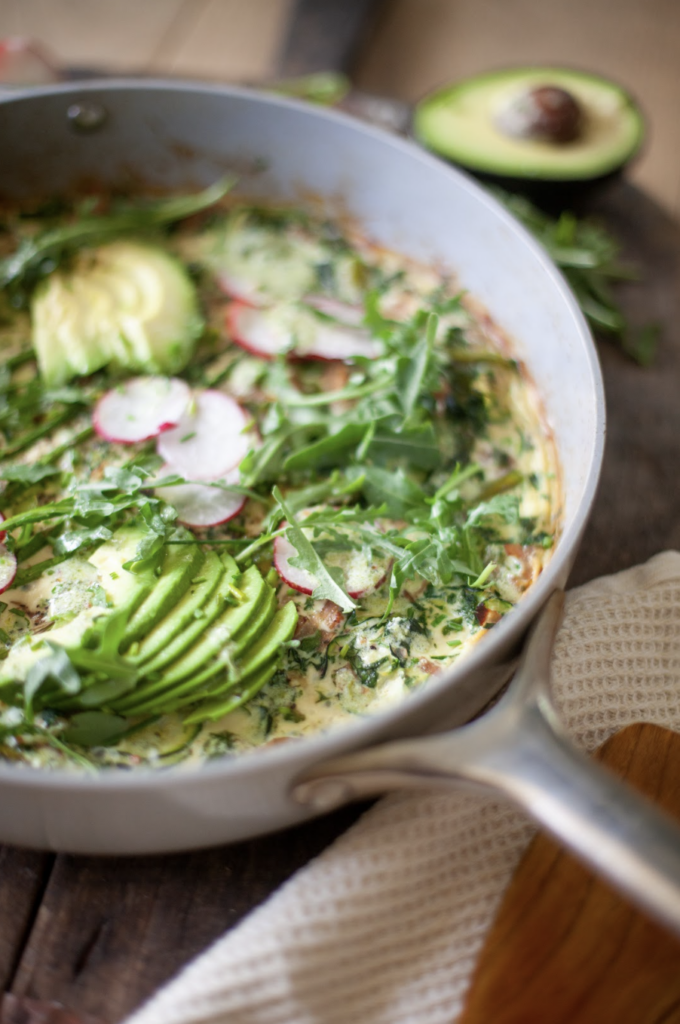 Spring frittata cooked in skillet and topped with arugula and avocado.