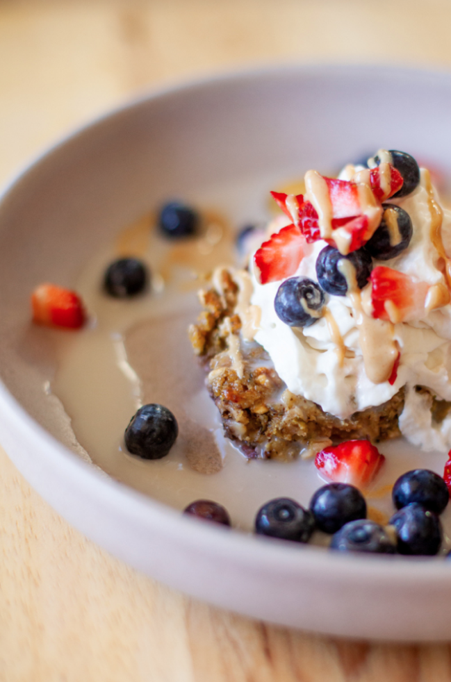 Lemon Blueberry Baked Zucchini Oats plated in a bowl with whip cream and fruit on top lillieeatsandtells.com
