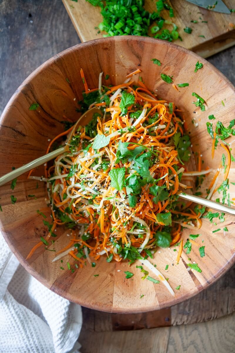 Cilantro being added to a large bowl full of carrot coleslaw.