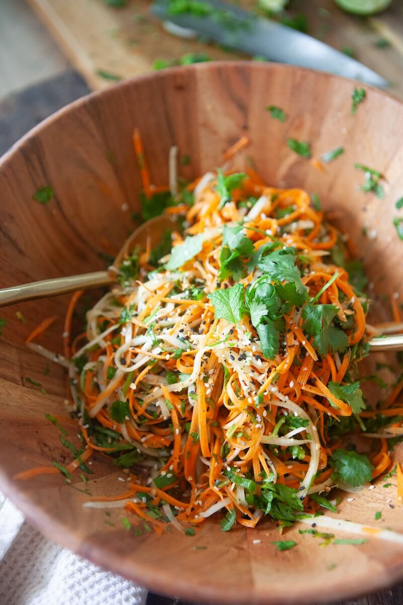 Thai carrot slaw being mixed in a wooden bowl.