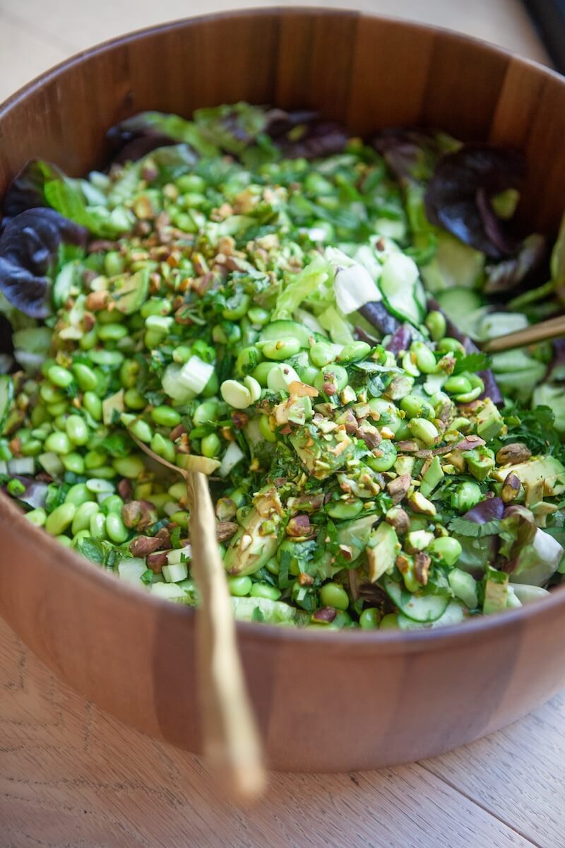 Green salad being tossed in a large wooden serving bowl.