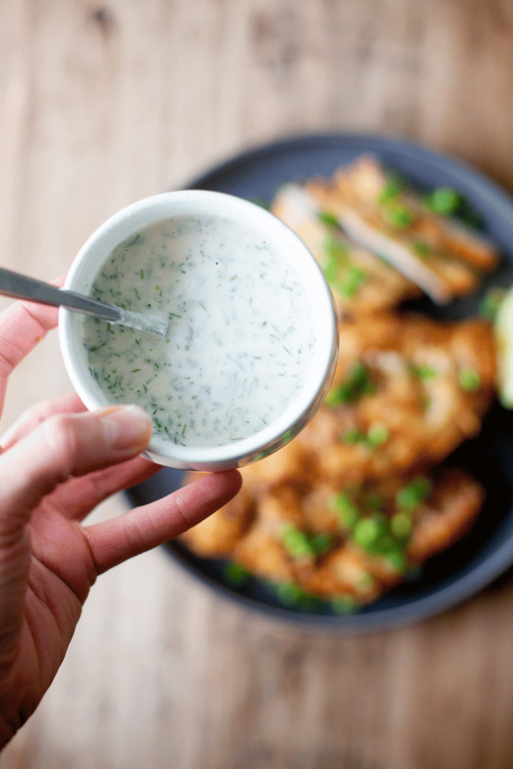 Herb yogurt dressing in a small bowl above a plate of chicken.