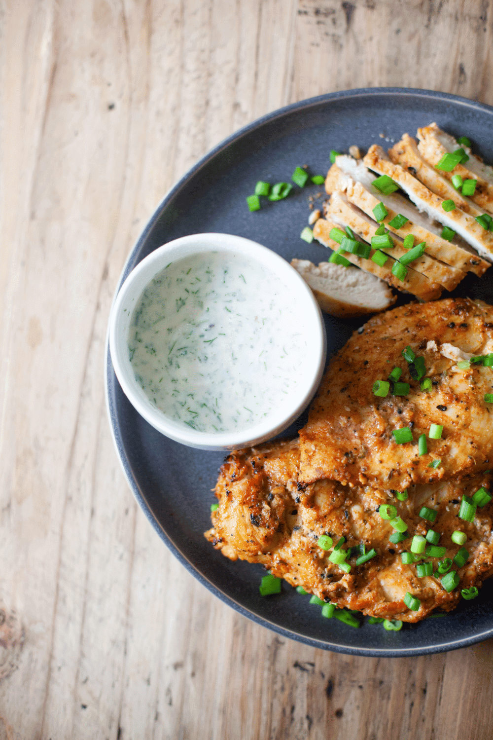 Herb yogurt dressing on a plate with sliced chicken.
