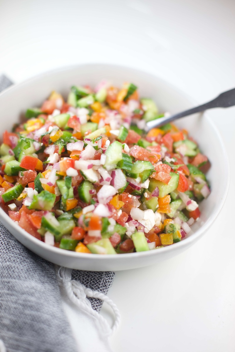 Up close image of Greek Salsa in a white bowl with a metal spoon sticking out of the bowl.