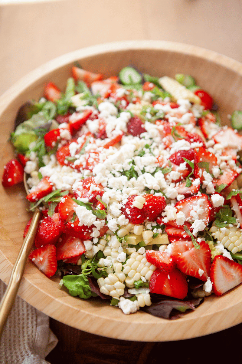 Ingredients for strawberry summer salad in a large wooden bowl.