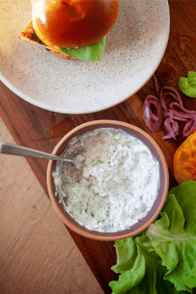 A bowl of tartar sauce on a wooden cutting board.