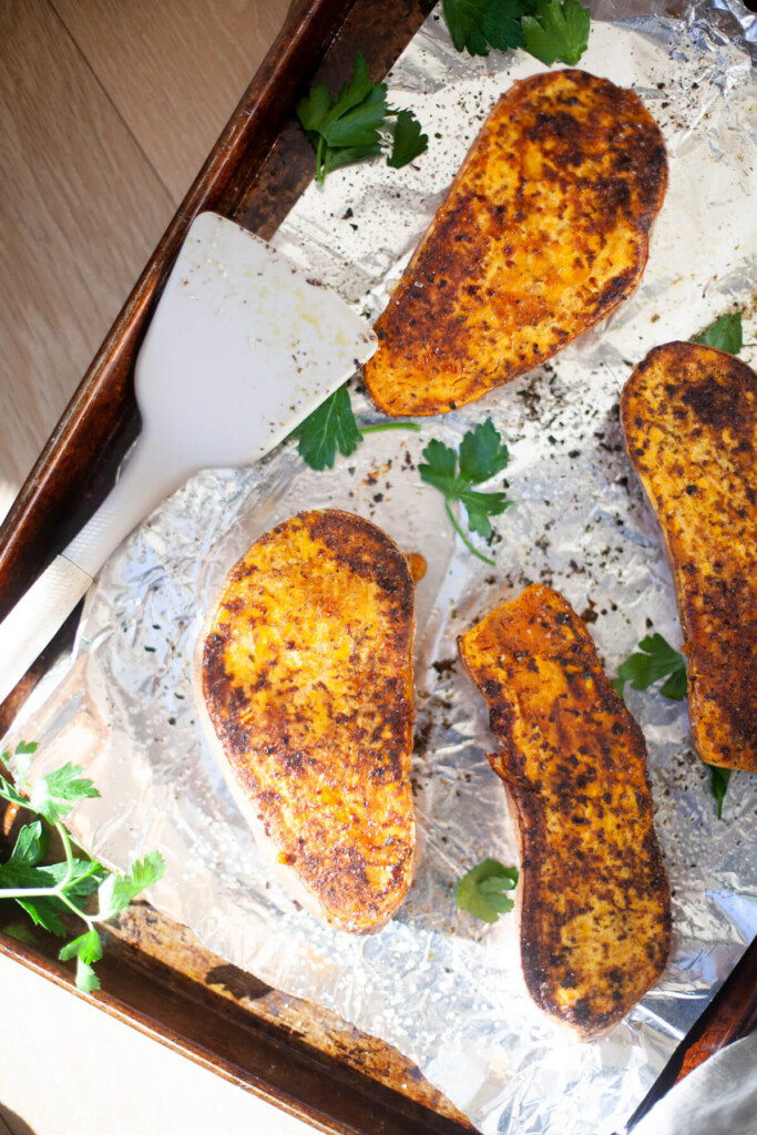 Sweet potatoes roasted on a pan with a white spatula.