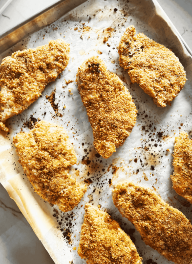 Seven pieces of baked breaded chicken on a baking sheet.